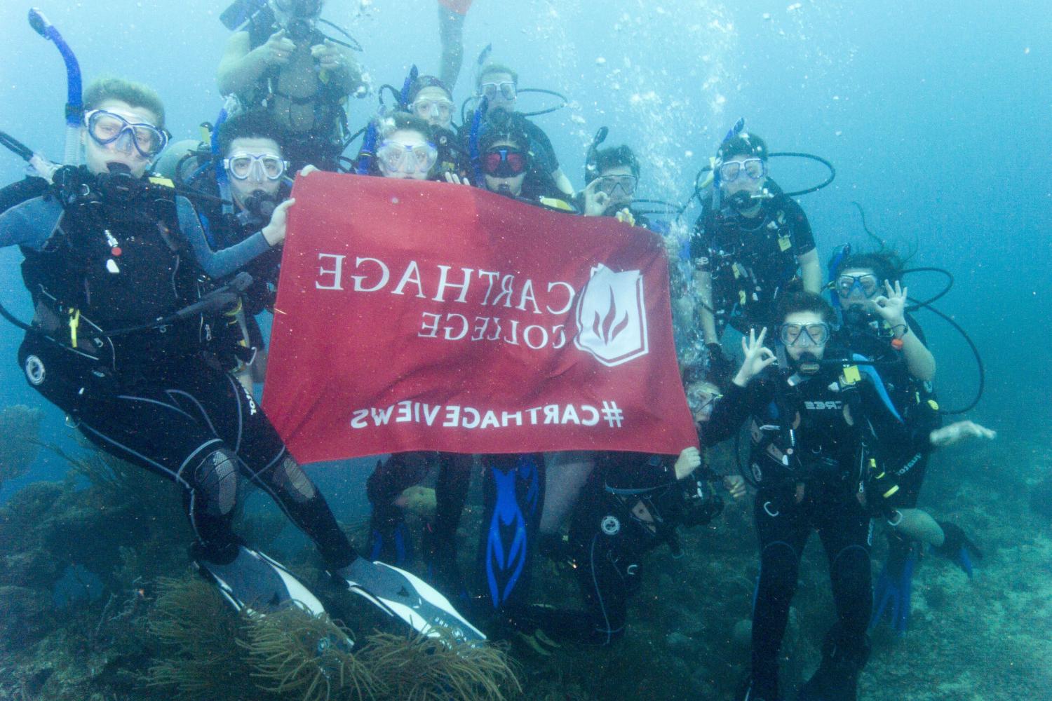 学生们手持<a href='http://udwuvuku.china-ads.net'>bv伟德ios下载</a>旗帜，在j学期洪都拉斯游学之旅中潜水.